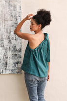 Woman wearing a teal top and blue jeans against a neutral wall.