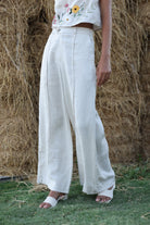 Person wearing white linen pants and a floral top standing in front of hay bales.