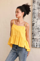 Woman wearing a yellow top and blue jeans against a beige wall.