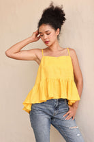Woman wearing a yellow tiered top and blue jeans against a beige background