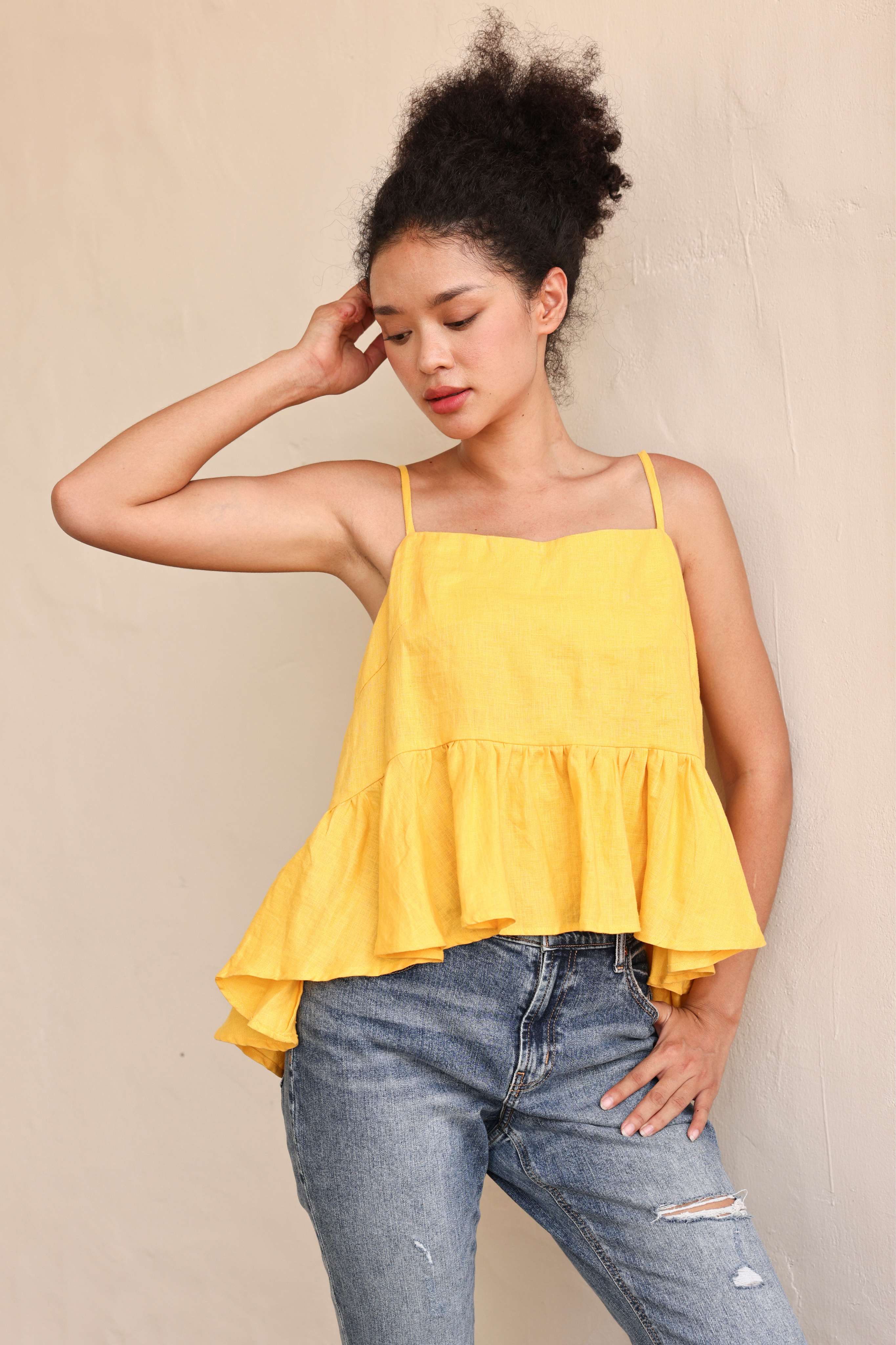 Woman wearing a yellow tiered top and blue jeans against a beige background