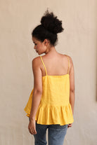 Woman wearing a yellow sleeveless top against a beige wall