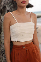 Woman wearing a beige top and rust-colored pants against a blurred natural background