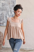 Woman wearing a top with ruffled sleeves and blue jeans against a neutral background