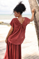 Woman in a rust-colored top standing by a palm tree on a beach.
