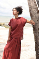 Woman in a red outfit leaning against a palm tree by the beach.