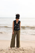 Woman standing on a beach wearing a sleeveless top with floral patterns and wide-leg pants.