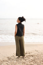 Woman standing on a beach wearing a black sleeveless top and green pants.