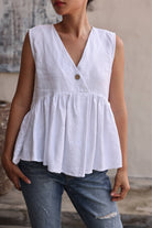 Person wearing a white sleeveless top with a V-neck and button detail, paired with blue jeans.