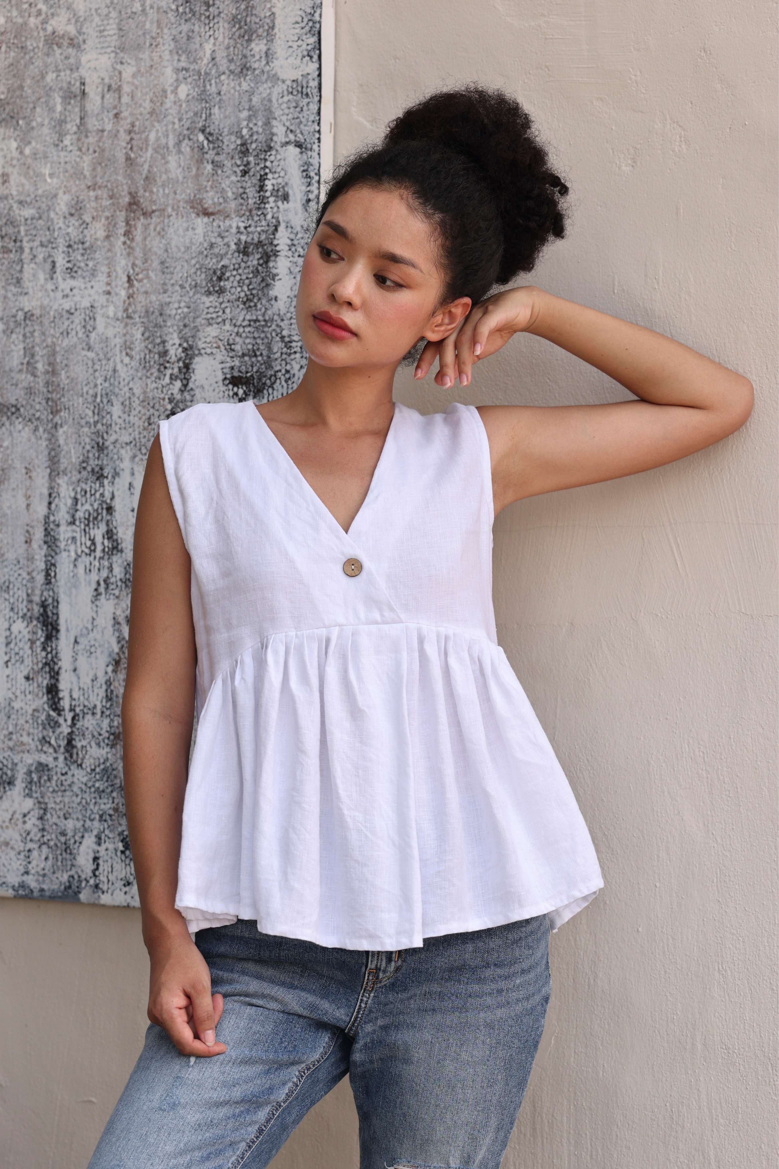 Woman wearing a white sleeveless top with a button and blue jeans against a textured wall.