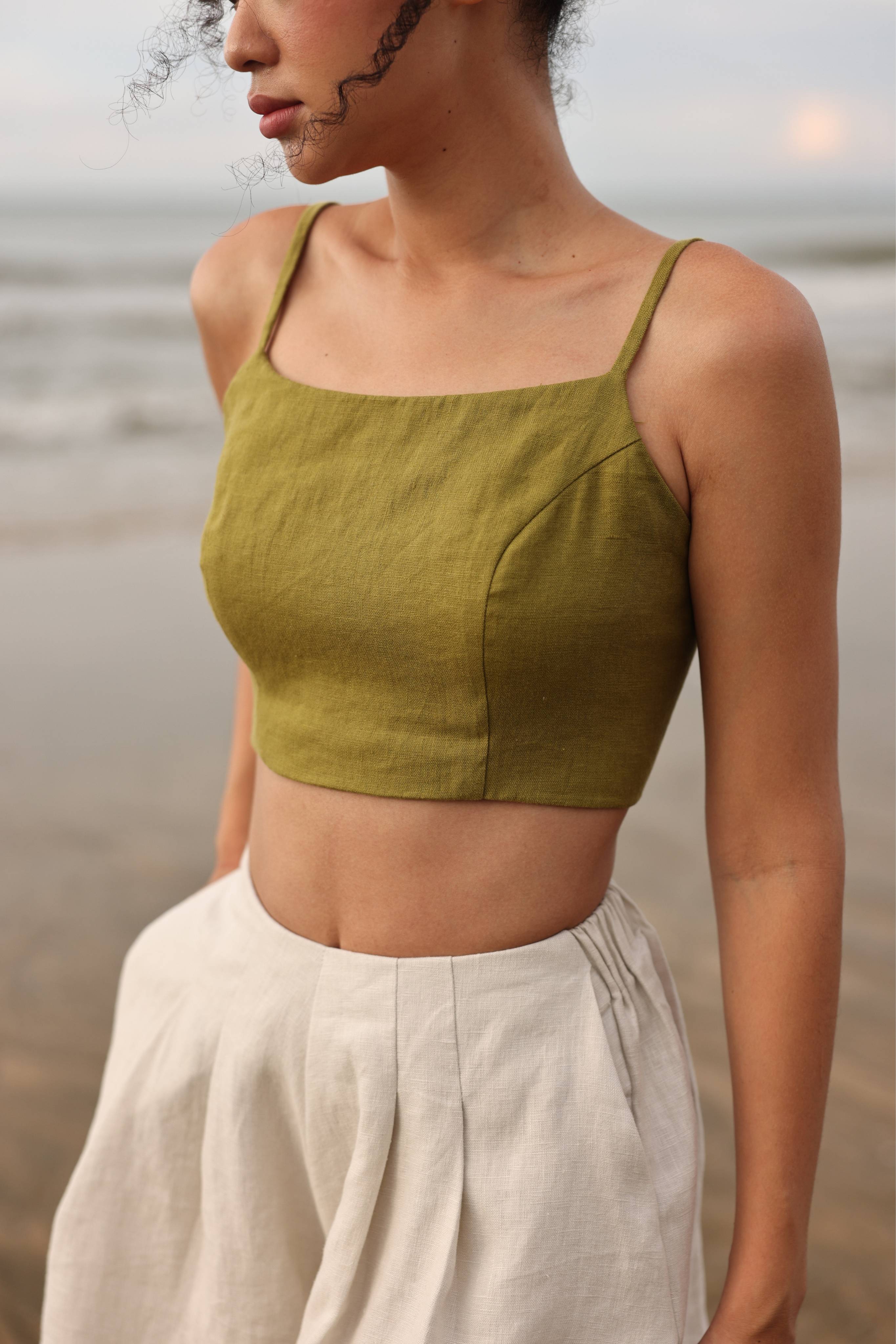 Woman wearing a green crop top and beige shorts on a beach.