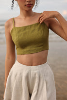 Woman wearing a green top and beige pants against a blurred natural background