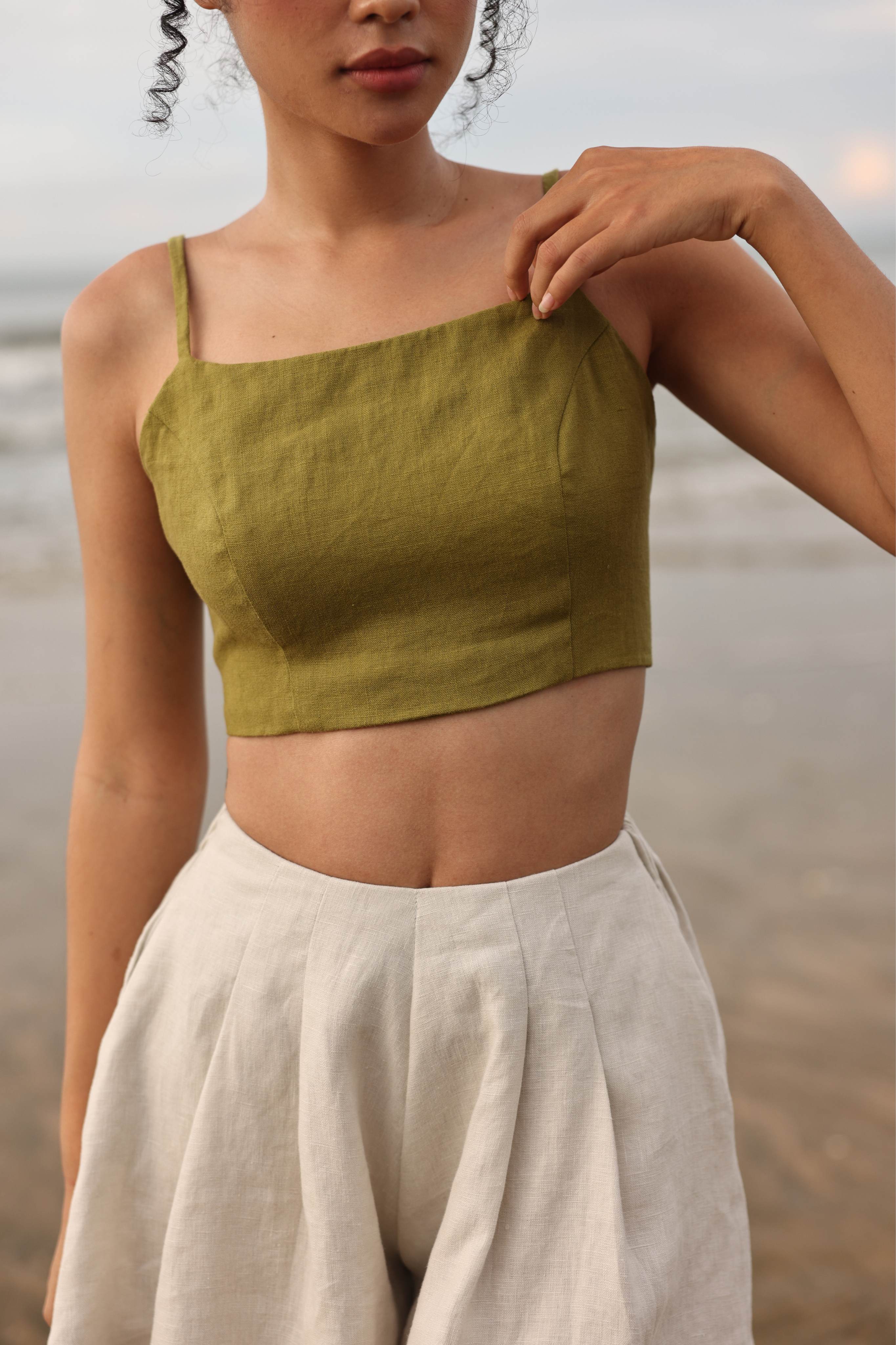 Woman wearing a green top and beige pants against a blurred natural background