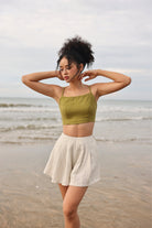 Woman standing on a beach wearing a green top and beige shorts.