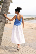Woman in a blue top and white skirt walking along a wooden boardwalk by the beach.