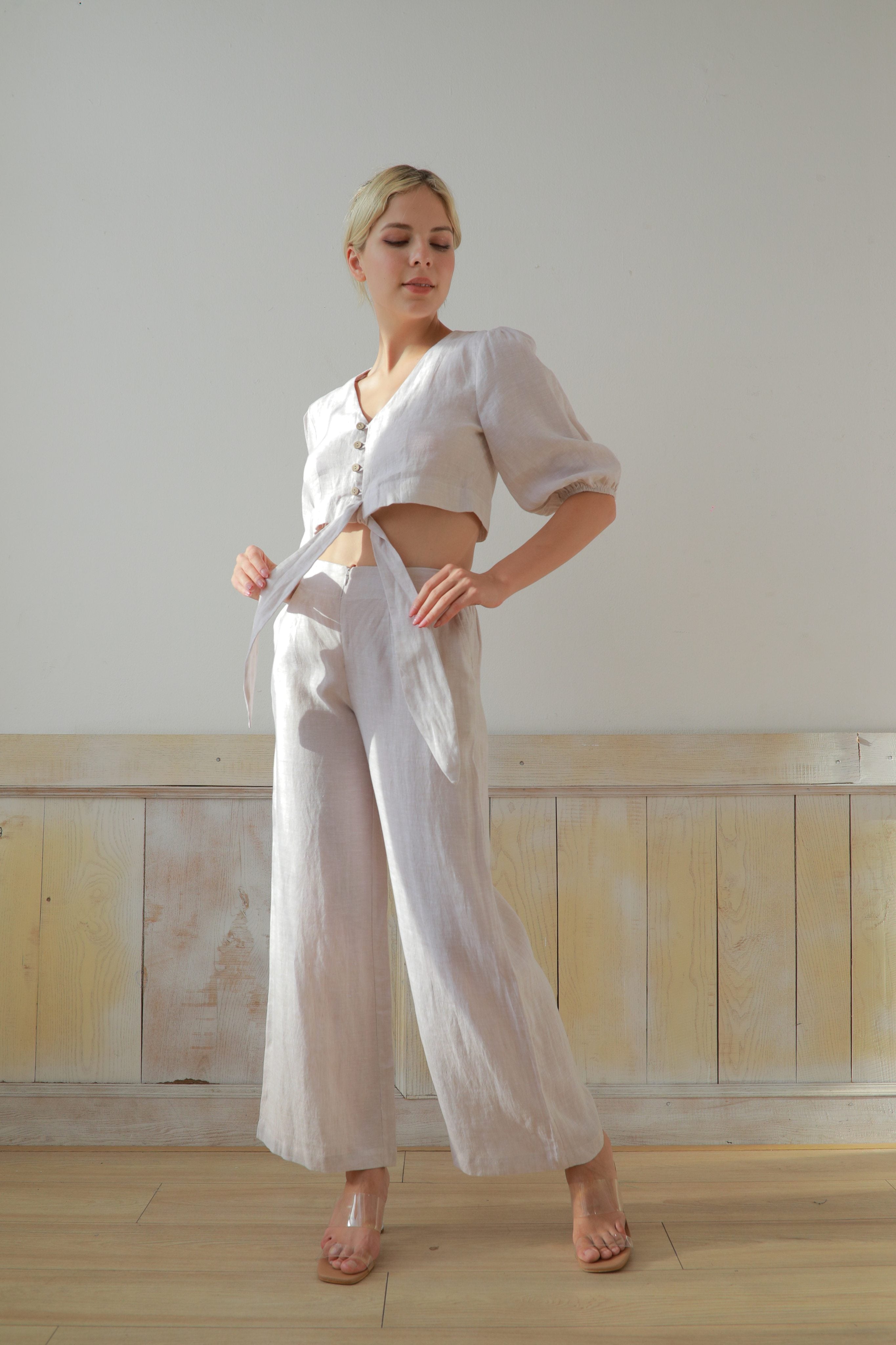 Woman wearing a white outfit standing against a light-colored wall.