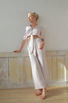 Woman in a white outfit standing against a light-colored wall.