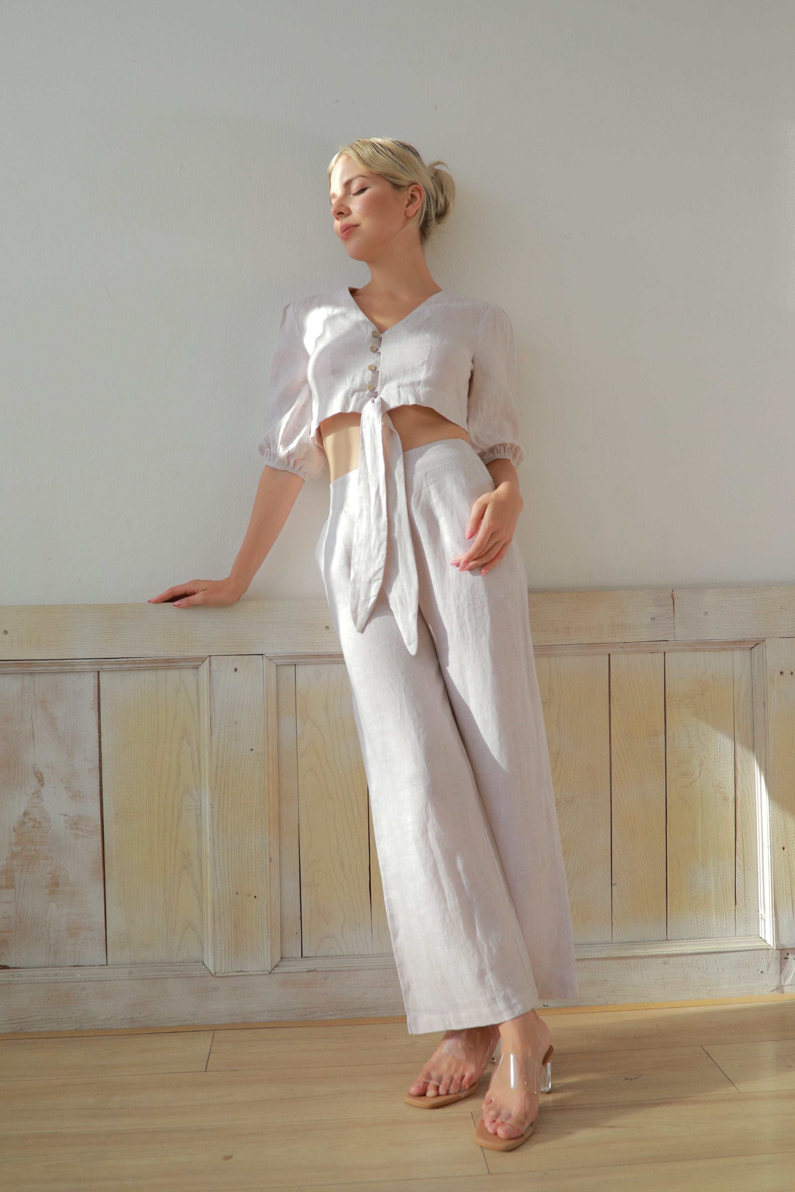 Woman in a white outfit standing against a light-colored wall.