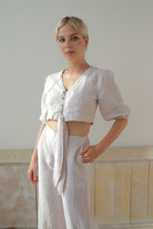 Woman wearing a white outfit standing against a plain wall.