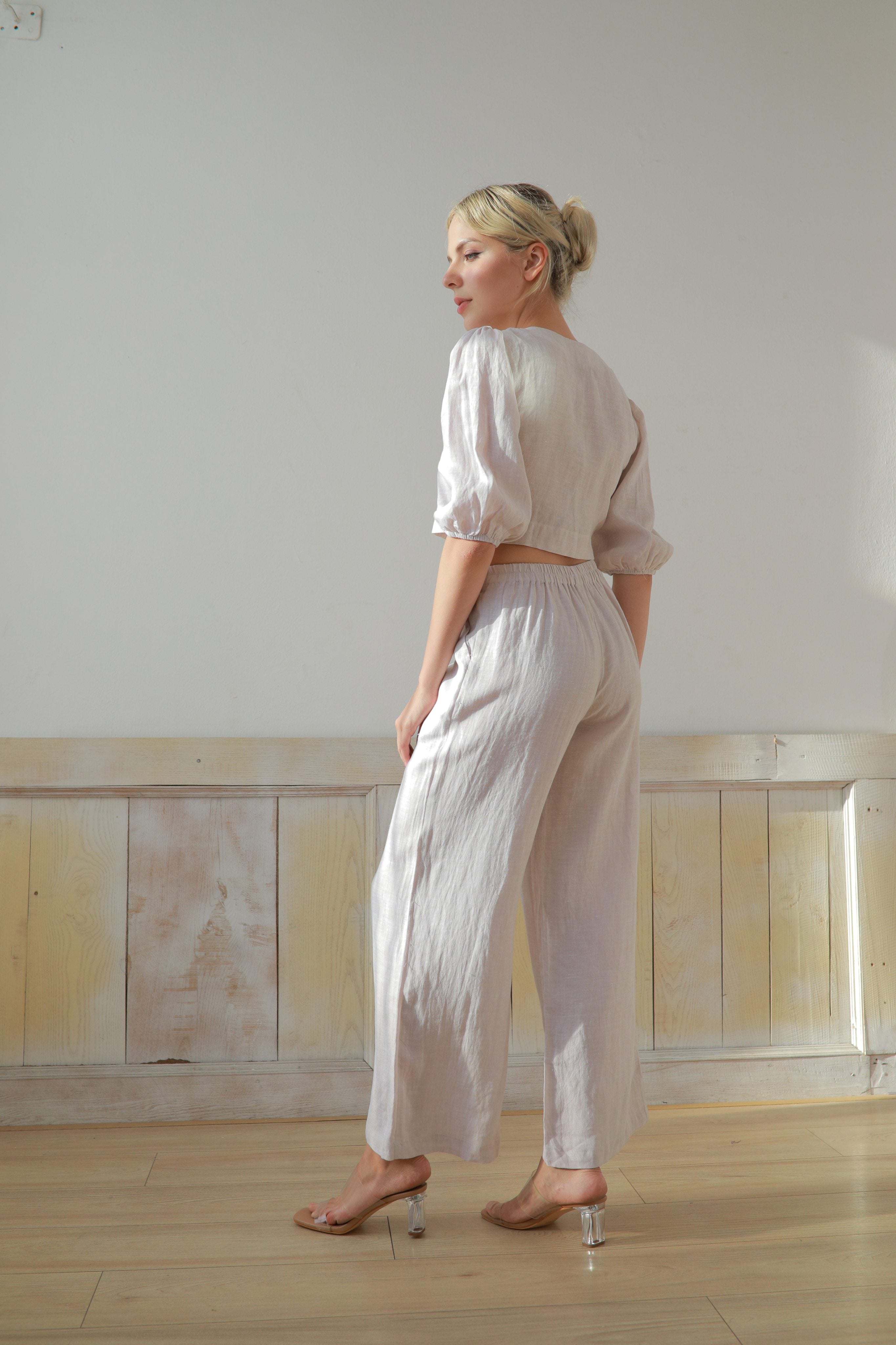 Woman wearing a white outfit standing in a room with wooden paneling.