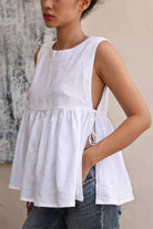 Person wearing a white sleeveless top with a plain background