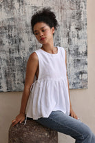 Woman wearing a white sleeveless top and jeans sitting on a textured surface with a patterned wall in the background.