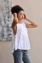 Woman wearing a white sleeveless top and blue jeans against a neutral wall.