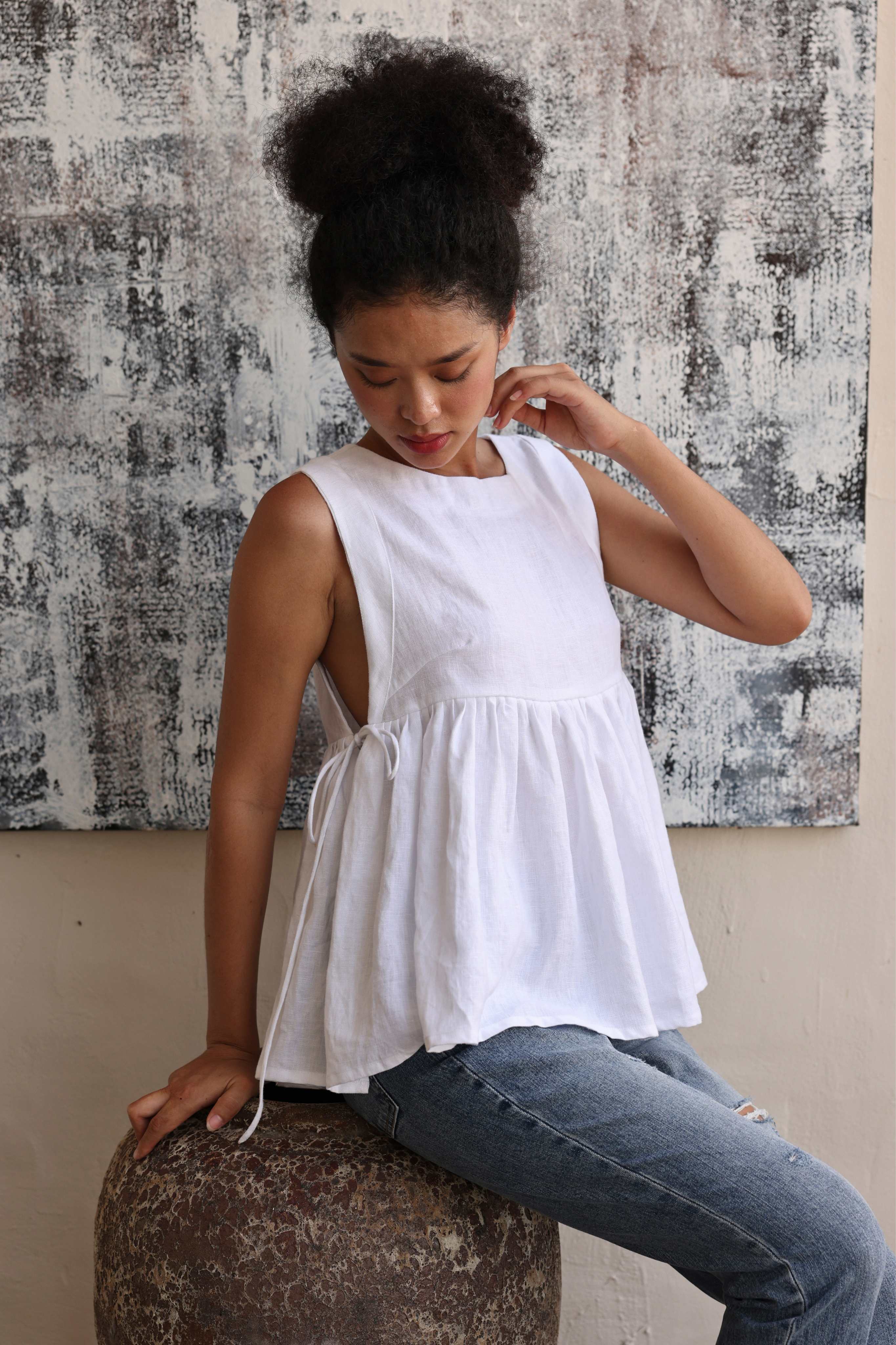 Woman wearing a white sleeveless top and blue jeans sitting on a textured surface.