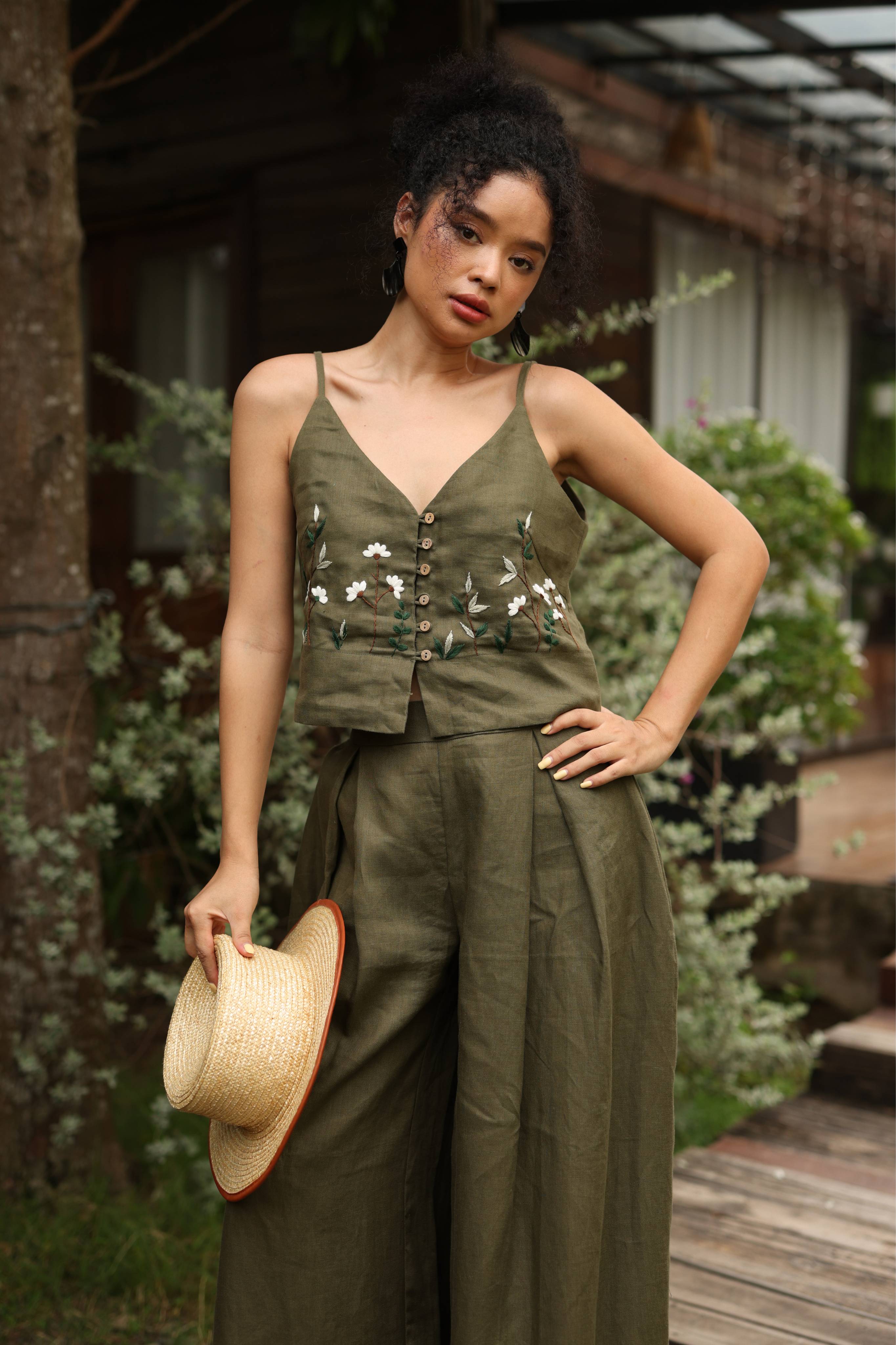 Woman in an olive green outfit holding a hat outdoors.