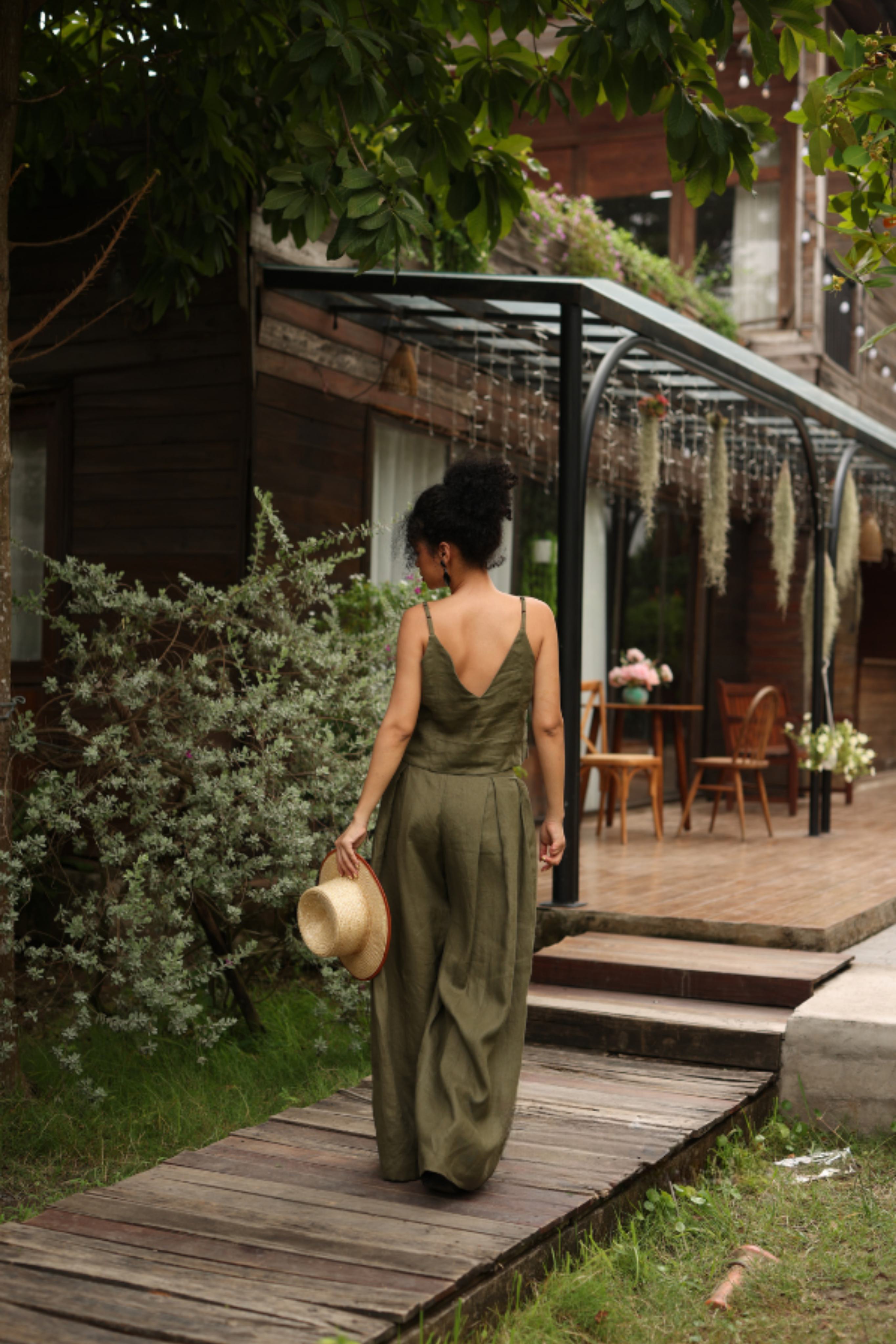 Woman in a green outfit walking on a wooden path in a garden setting.