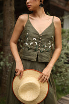 Woman wearing a green floral top and holding a straw hat outdoors.