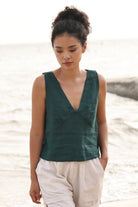 Woman wearing a green sleeveless top and beige shorts standing on a beach.