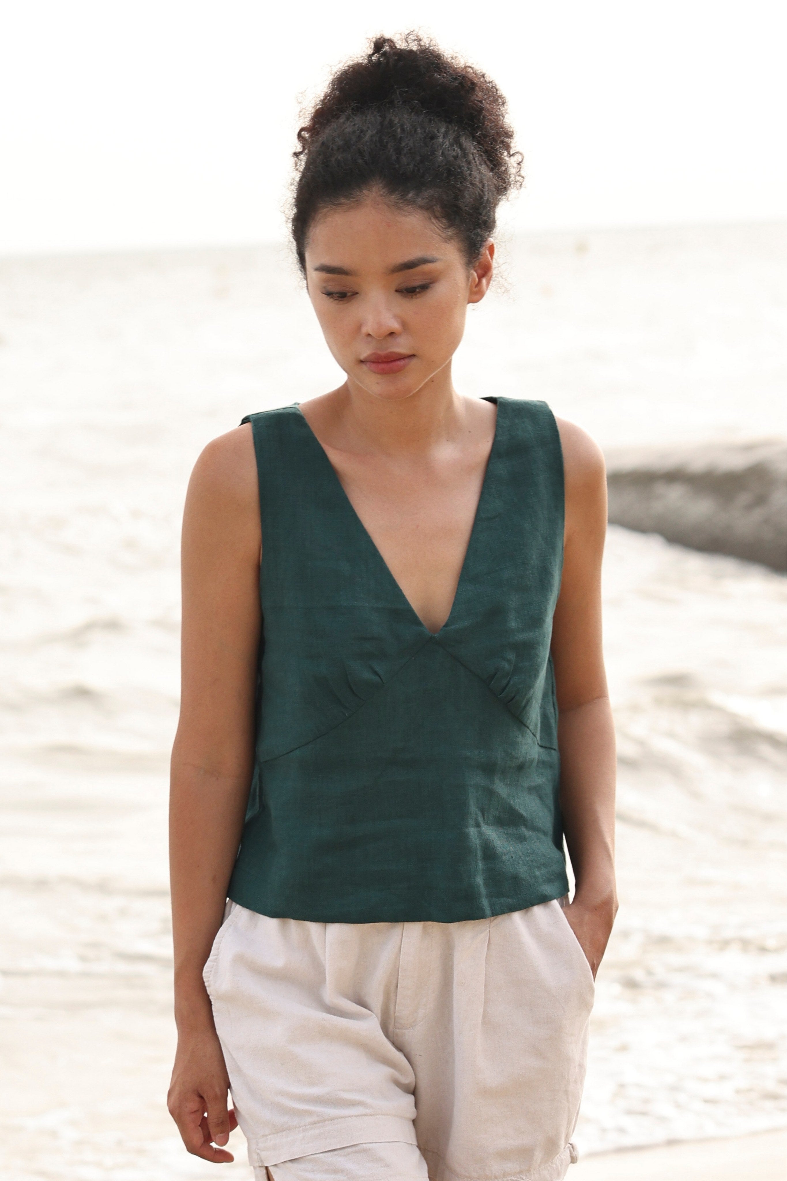 Woman wearing a green sleeveless top and beige shorts standing on a beach.