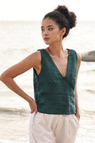 Woman wearing a green sleeveless top and beige shorts standing by a body of water.