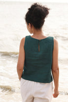 Person wearing a green sleeveless top and beige shorts standing by a body of water.