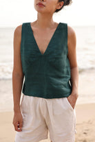 Woman wearing a green sleeveless top and beige shorts on a beach.