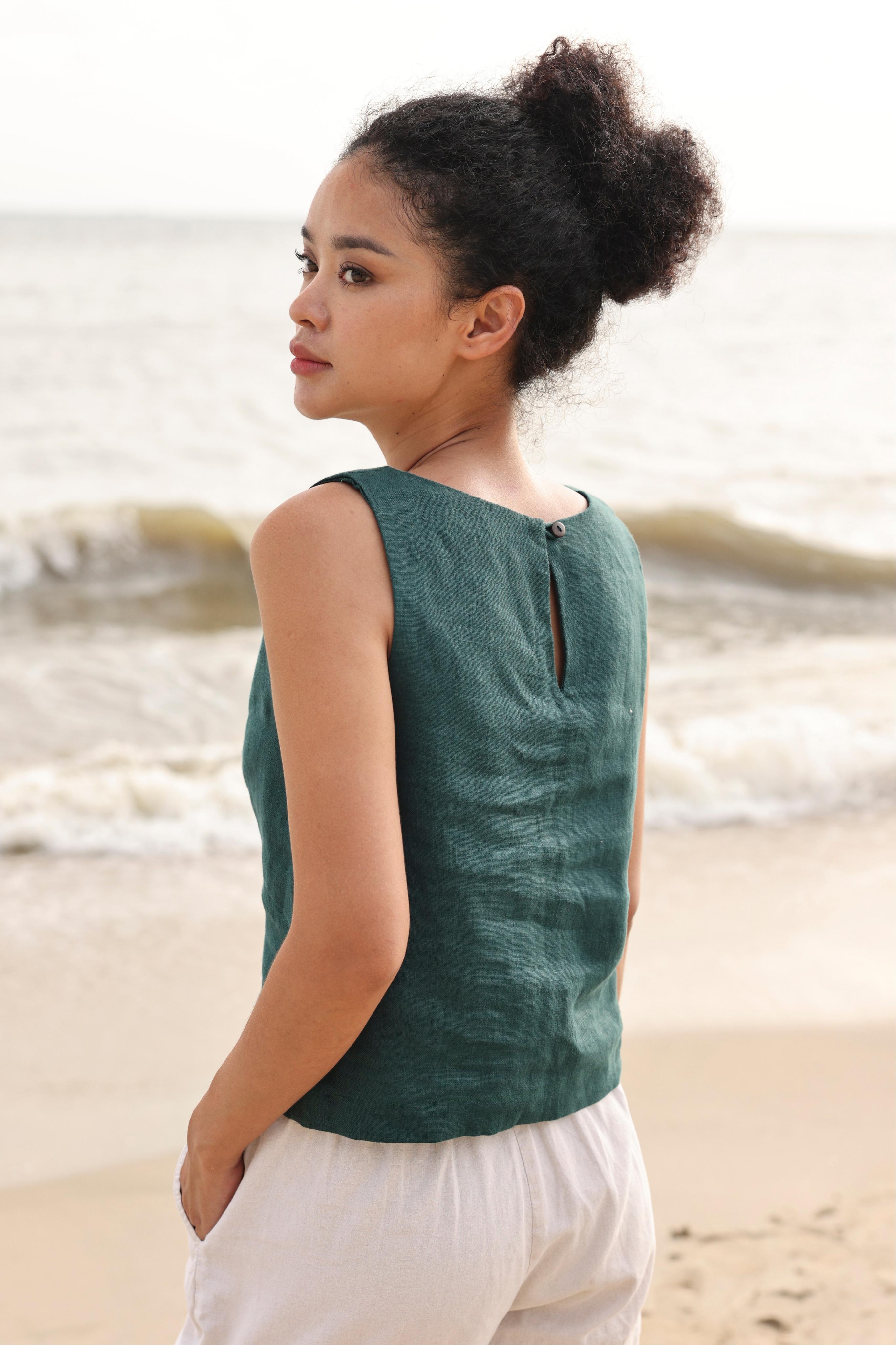 Woman wearing a green sleeveless top and beige shorts standing on a beach.