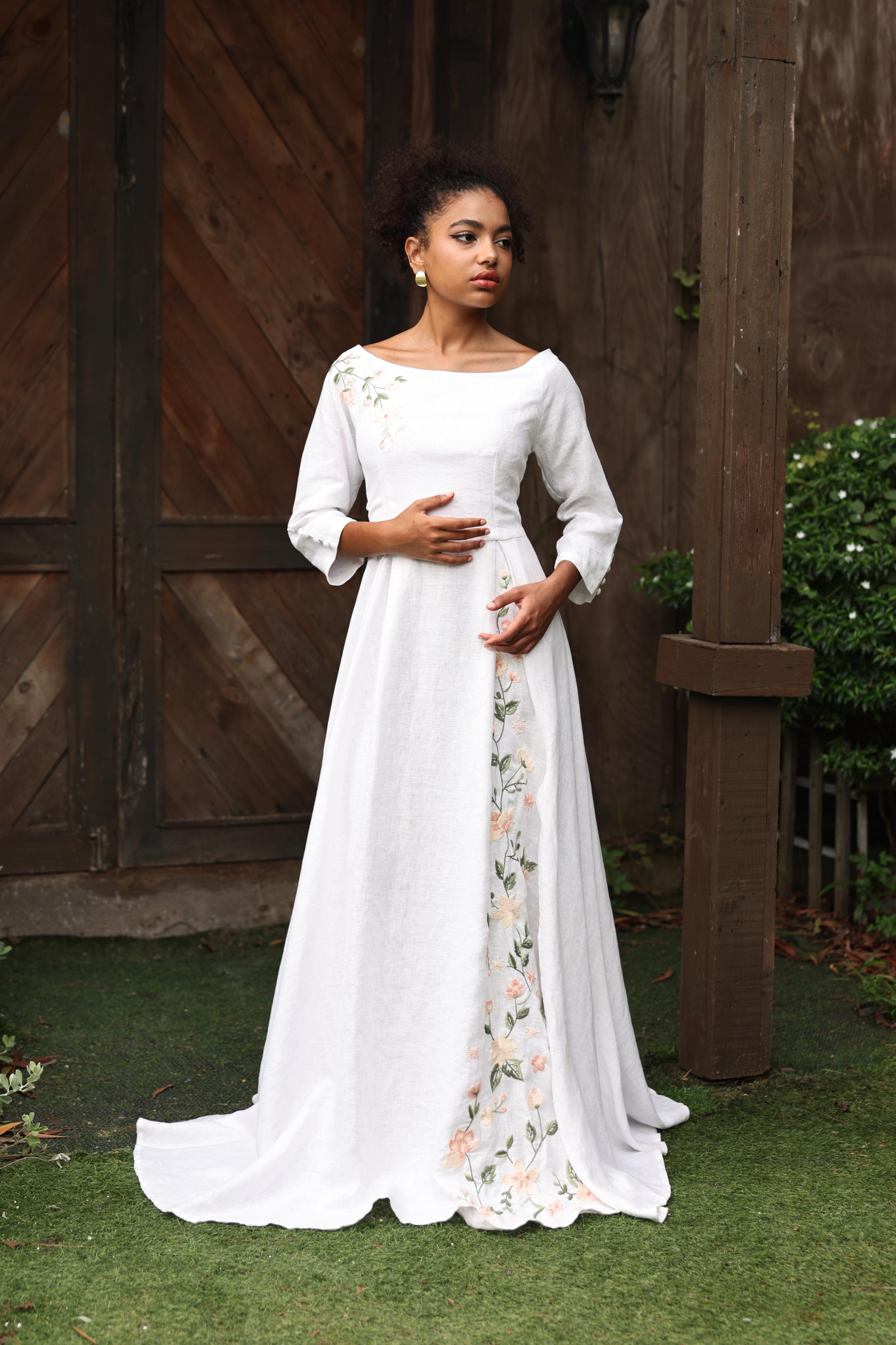Woman wearing a white dress with floral patterns standing outdoors.