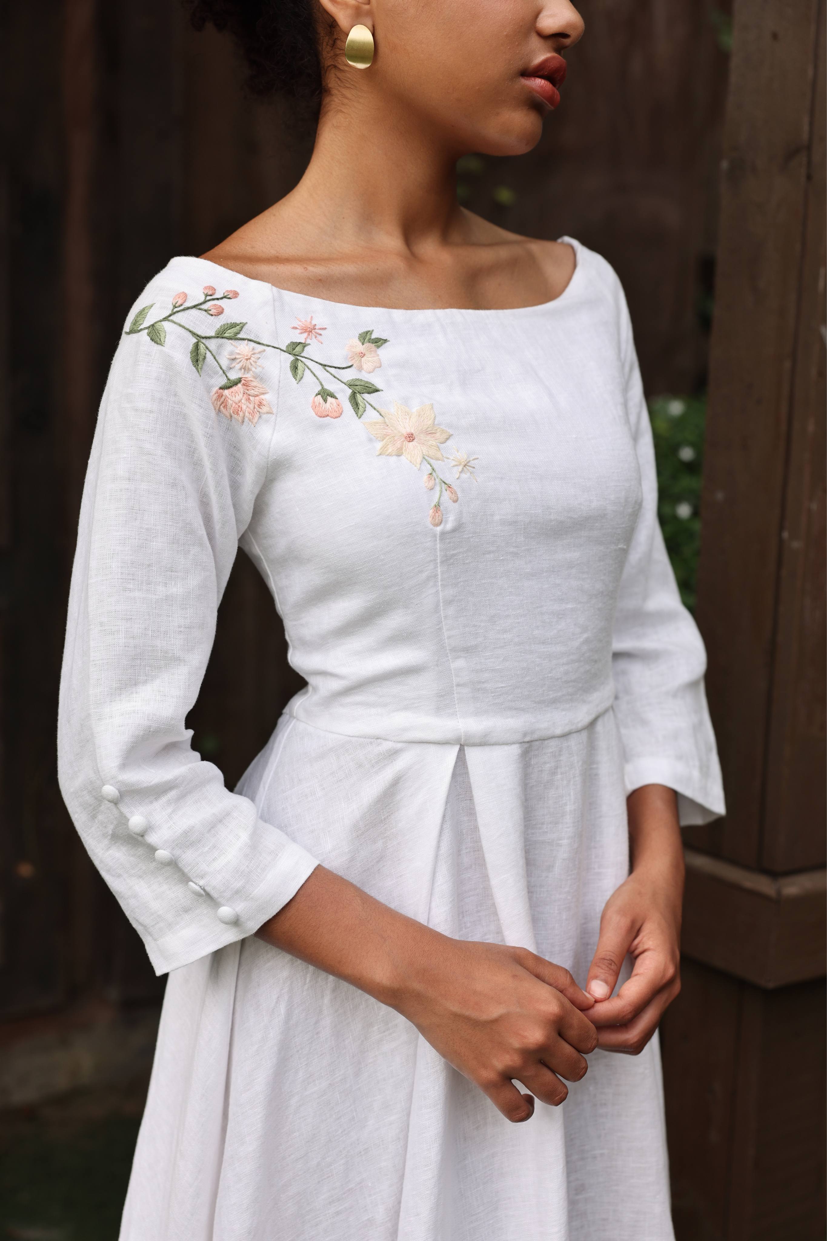 White dress with floral embroidery on 3/4 sleeves worn by a person.