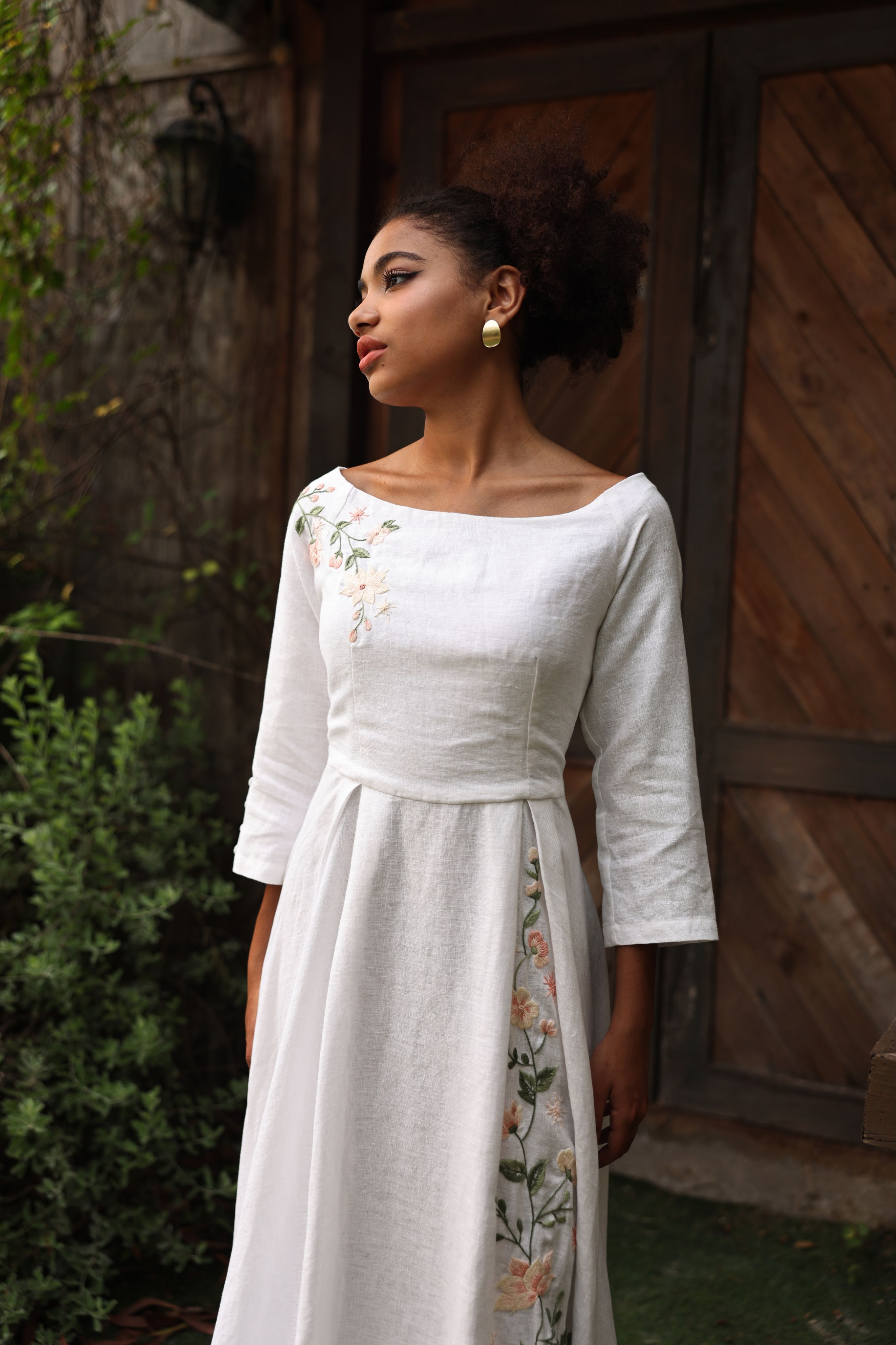 Woman wearing a white dress with floral patterns standing in front of a wooden door.