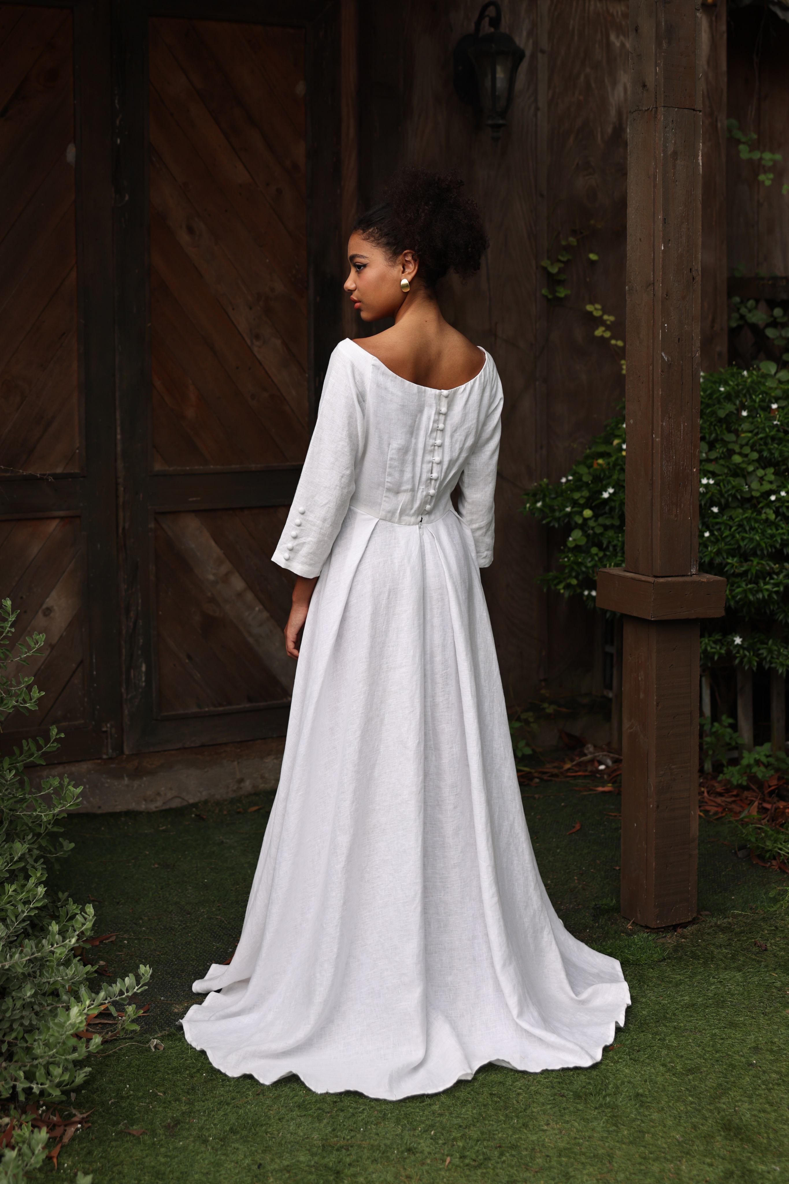 Woman in a white dress standing outdoors with wooden doors in the background