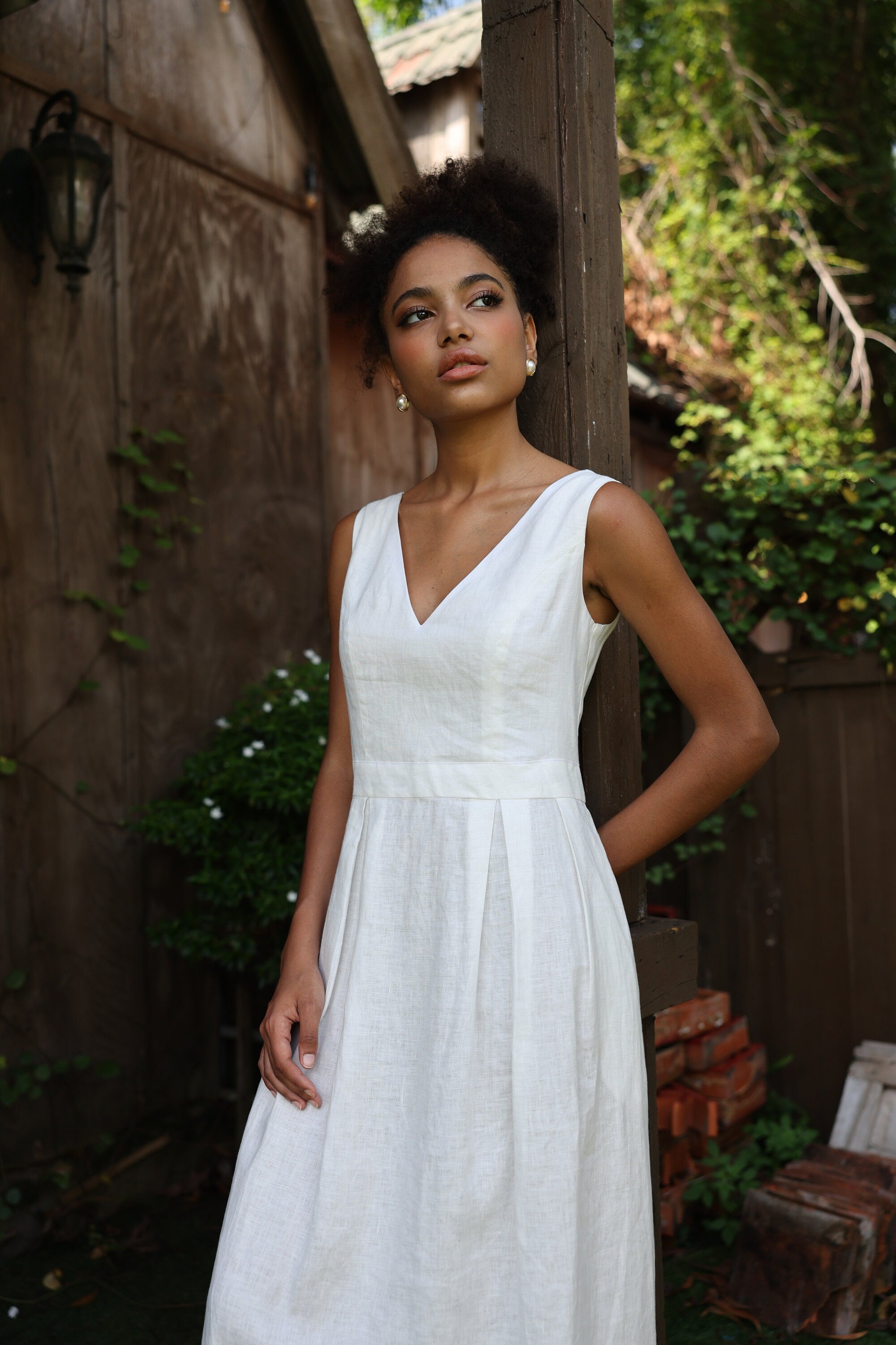 Woman in an ivory dress standing outdoors with greenery in the background