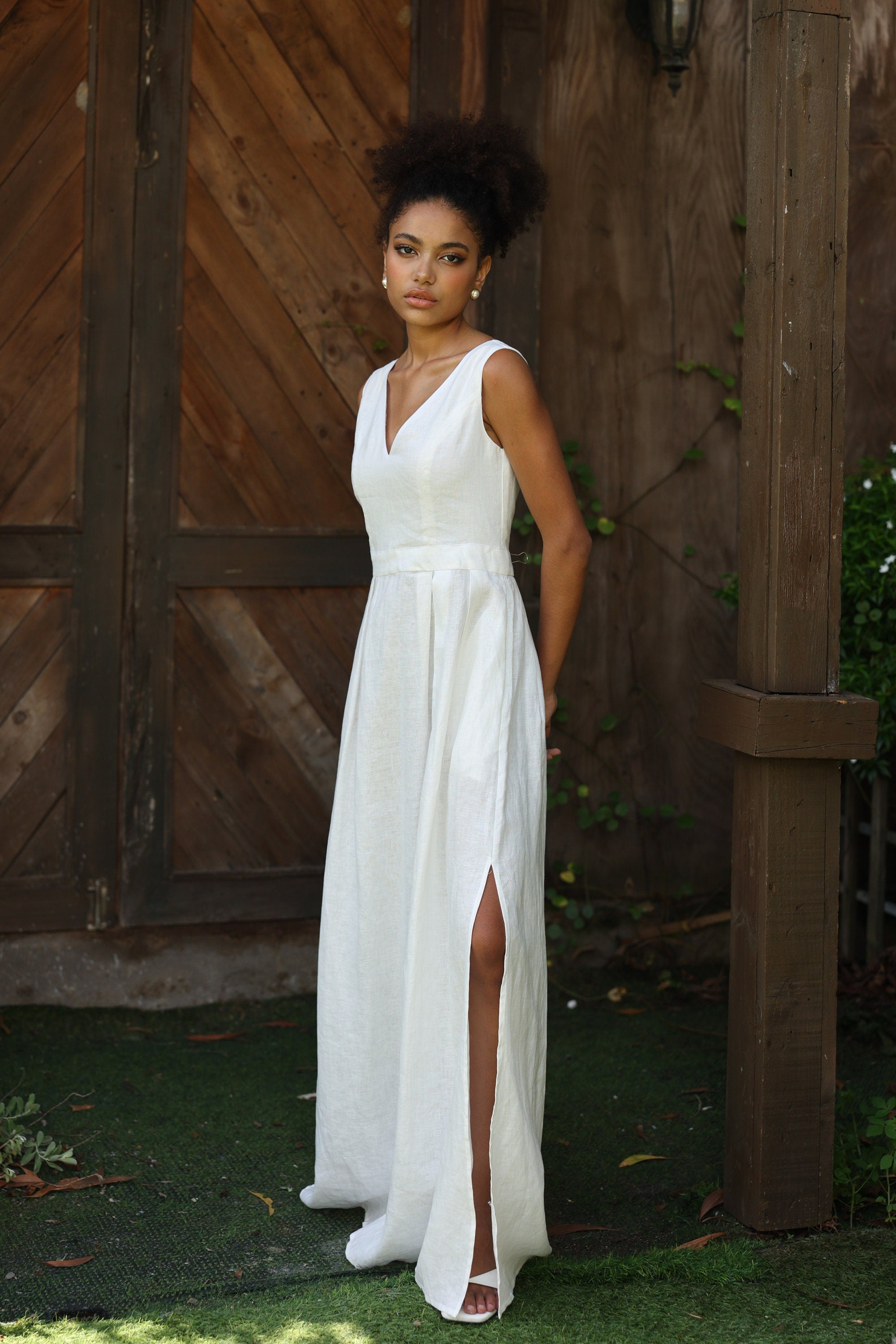 Woman in an ivory dress standing against a wooden wall.