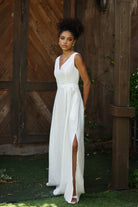 Woman in an ivory dress standing against a wooden wall.