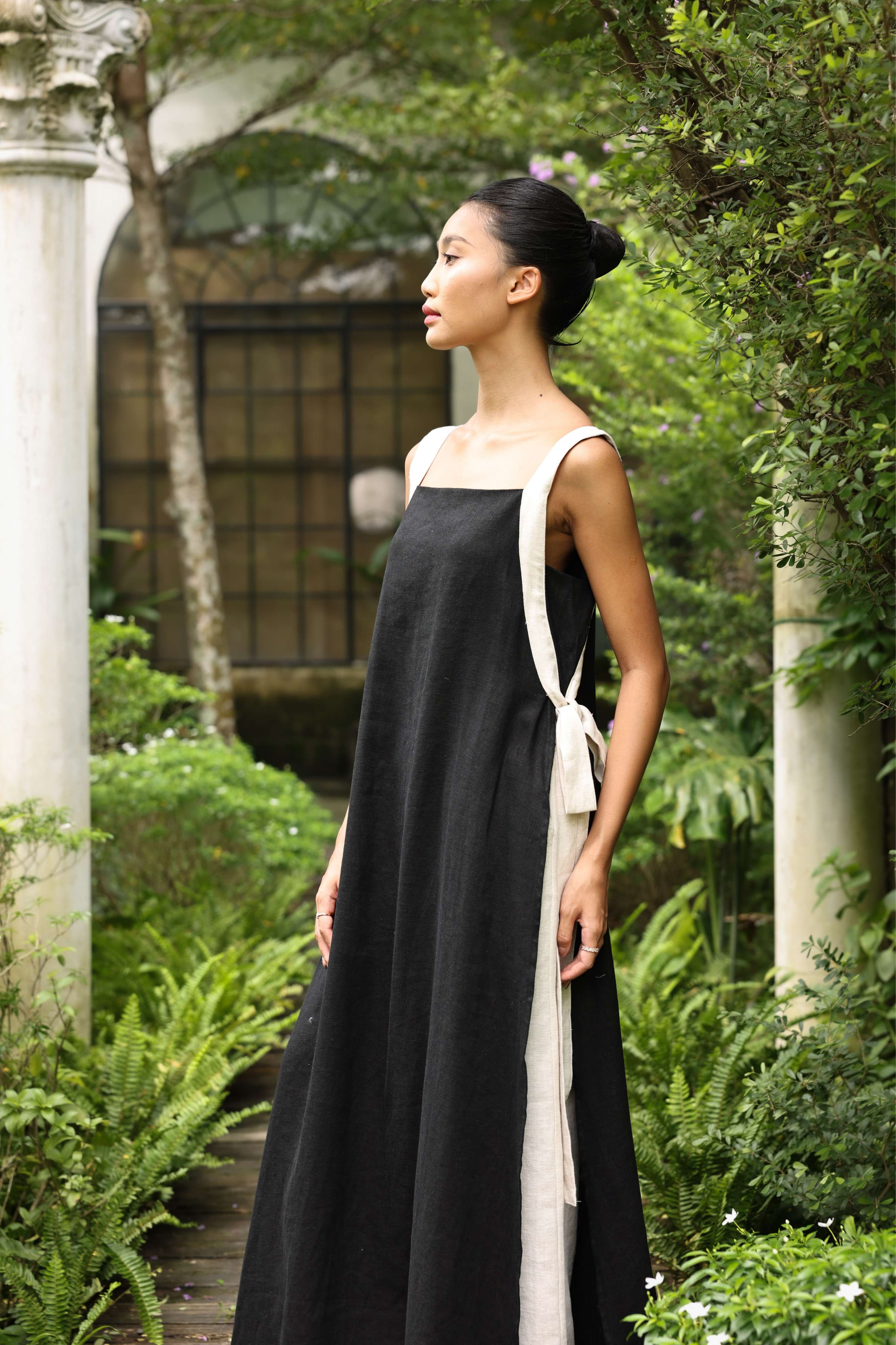 Woman in a black dress with white straps standing in a garden setting