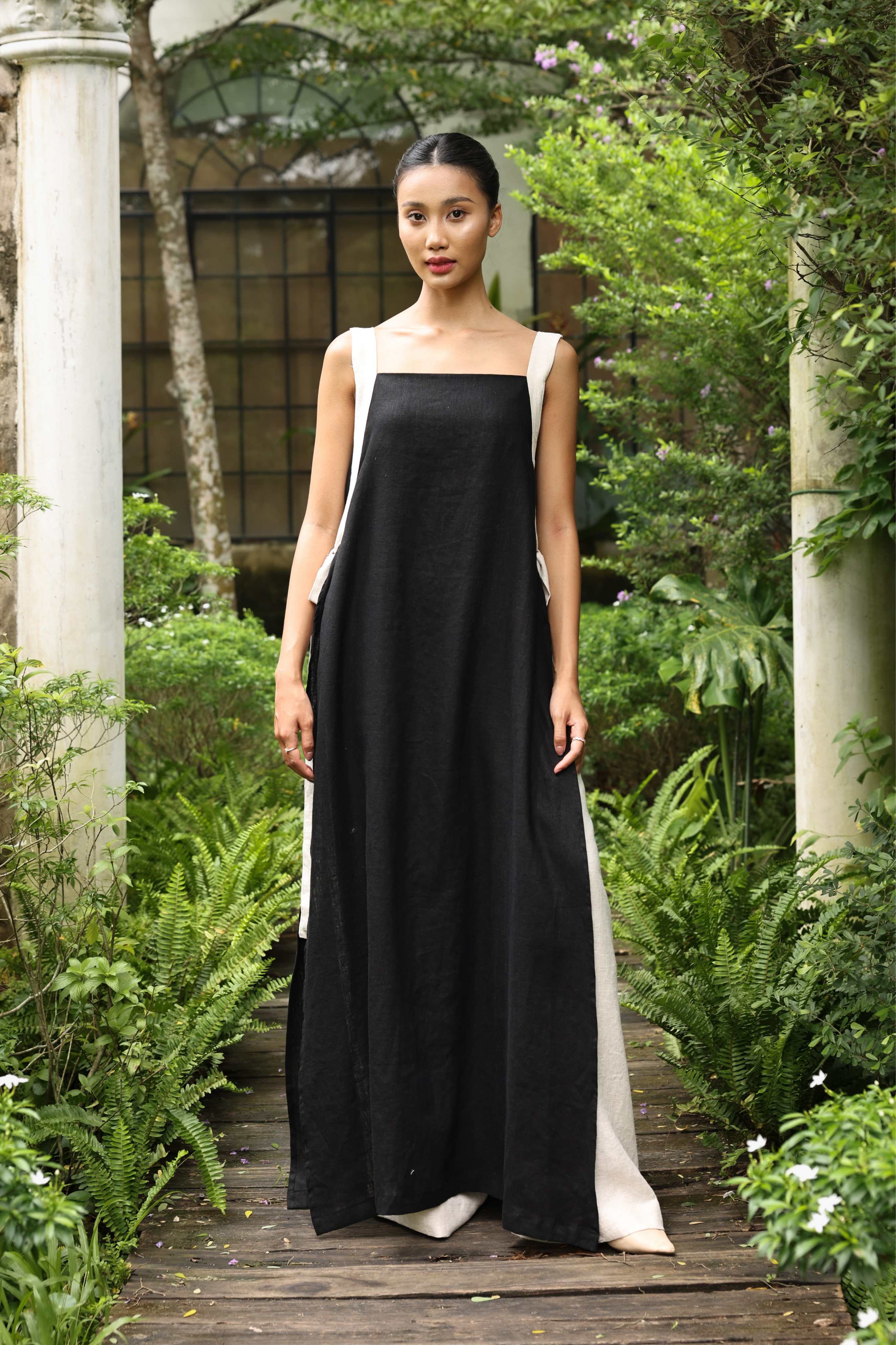 Woman in a black dress standing on a wooden path with greenery around