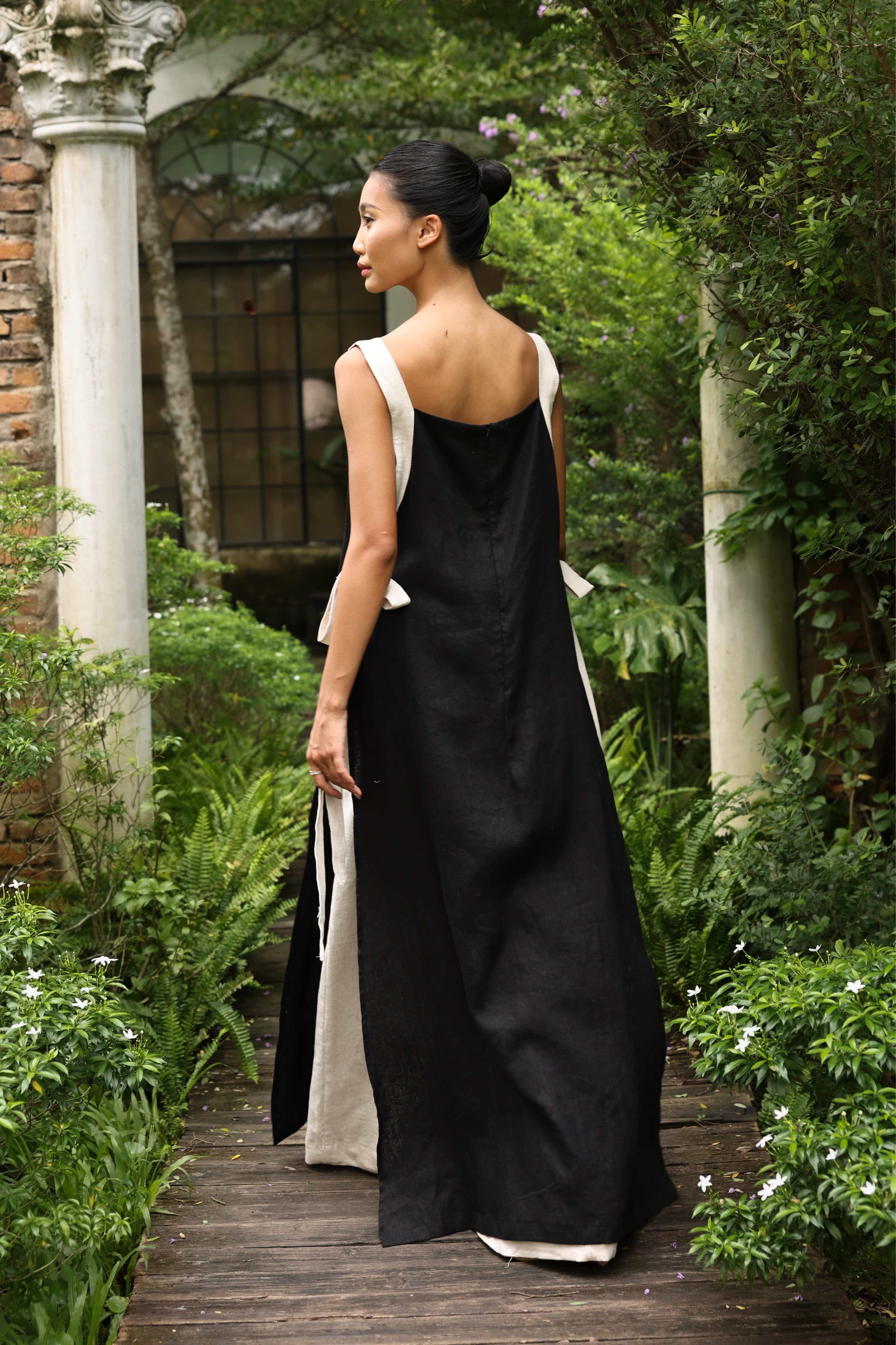 Woman in a black dress with white straps walking through a garden.
