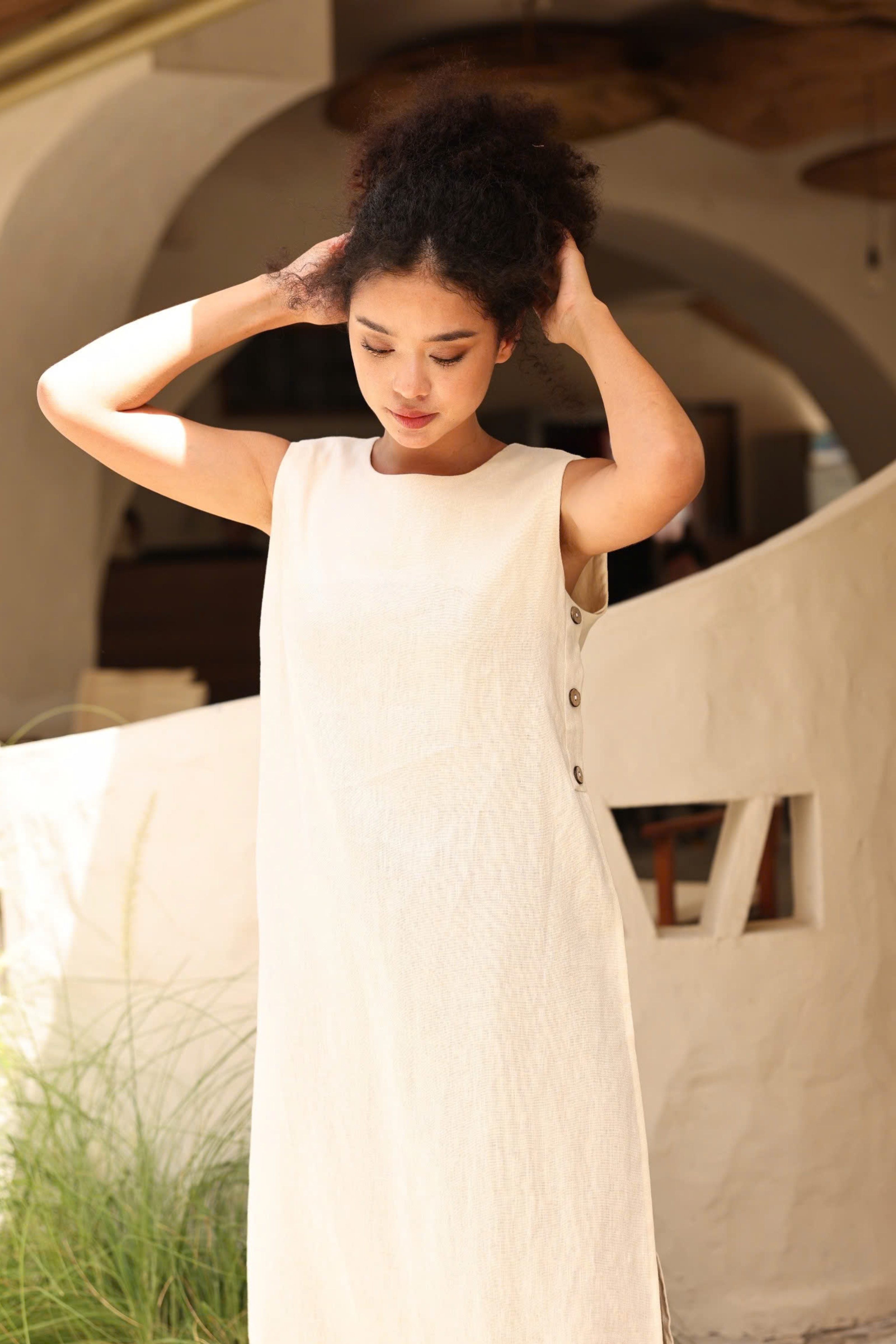 Woman in a white dress standing in an outdoor setting with architectural elements.