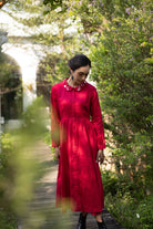 Woman in a red dress standing in a natural setting with greenery and a blurred background