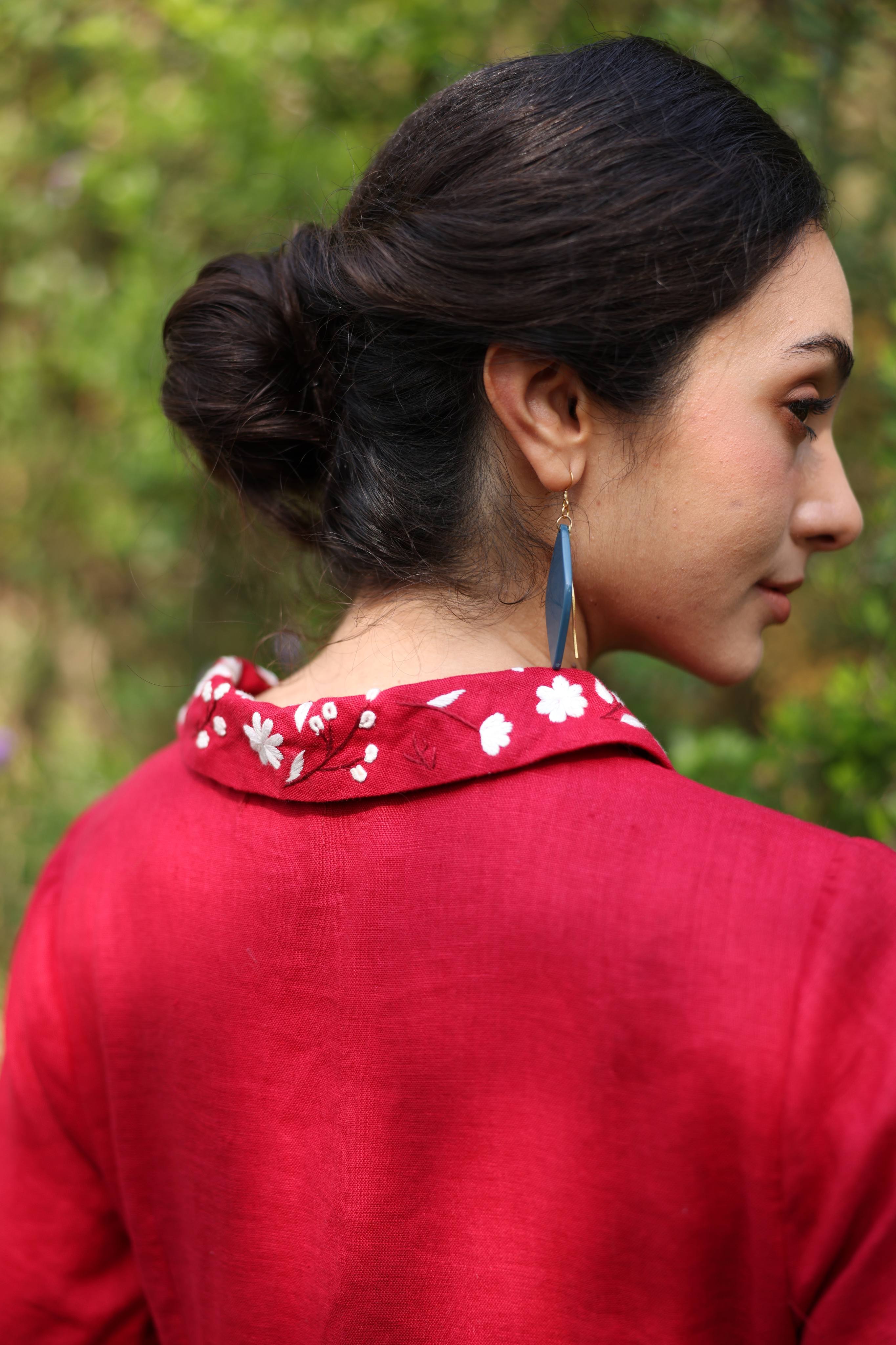 Woman wearing a red dress with floral collar, looking over her shoulder with a blurred green background